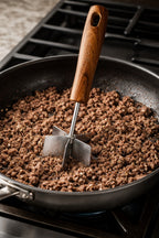 Walnut-handle stainless steel meat chopper crumbling ground beef in a nonstick pan