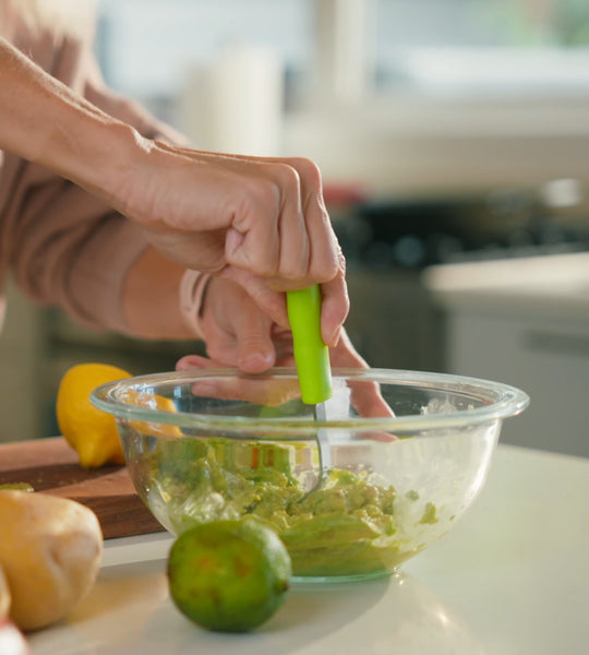 Hands mashing avocado into guacamole in a glass bowl with the Mini Masher